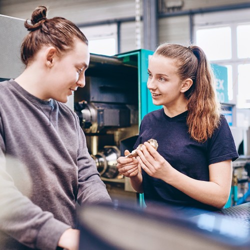 Two young an female trainees talking about a copper component
