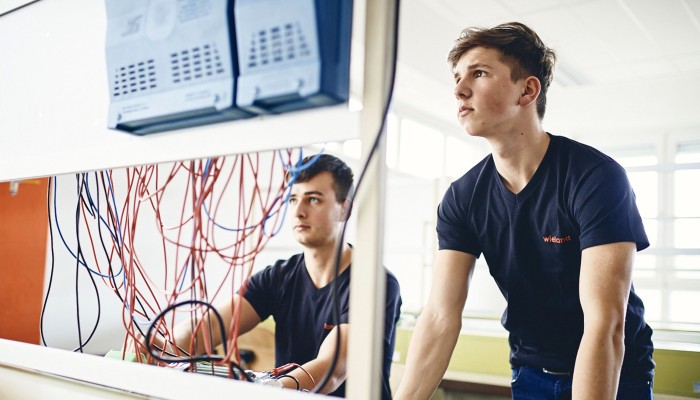 Trainee Noah standing in front of a computer together with his co-worker