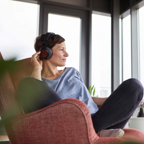 Woman with headphones sitting in armchair looking out auf the window