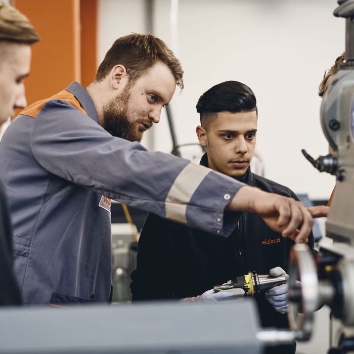 Production specialist showing two trainees how to work on a machine