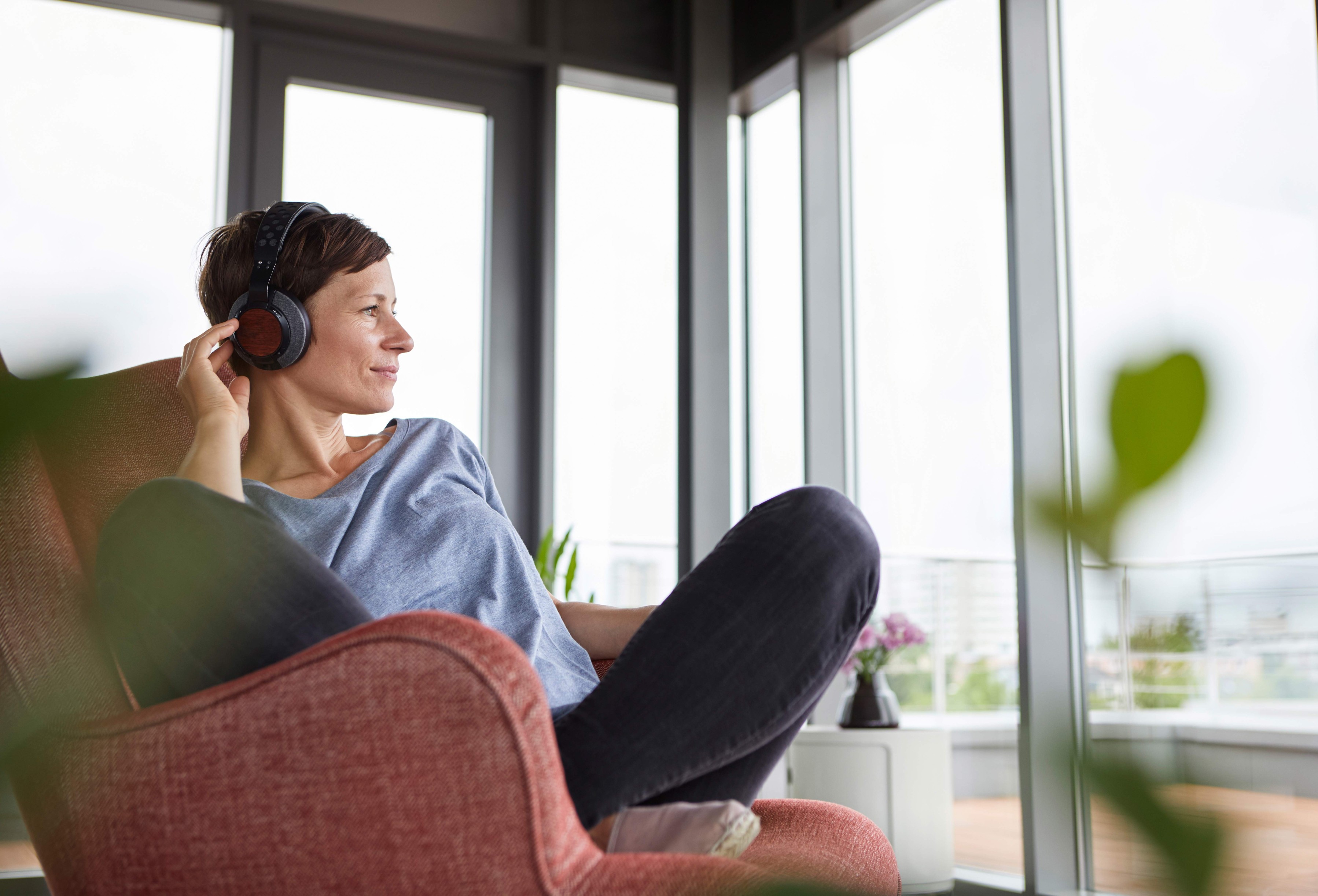 Woman with headphones sitting in an arm chair looking out of the window