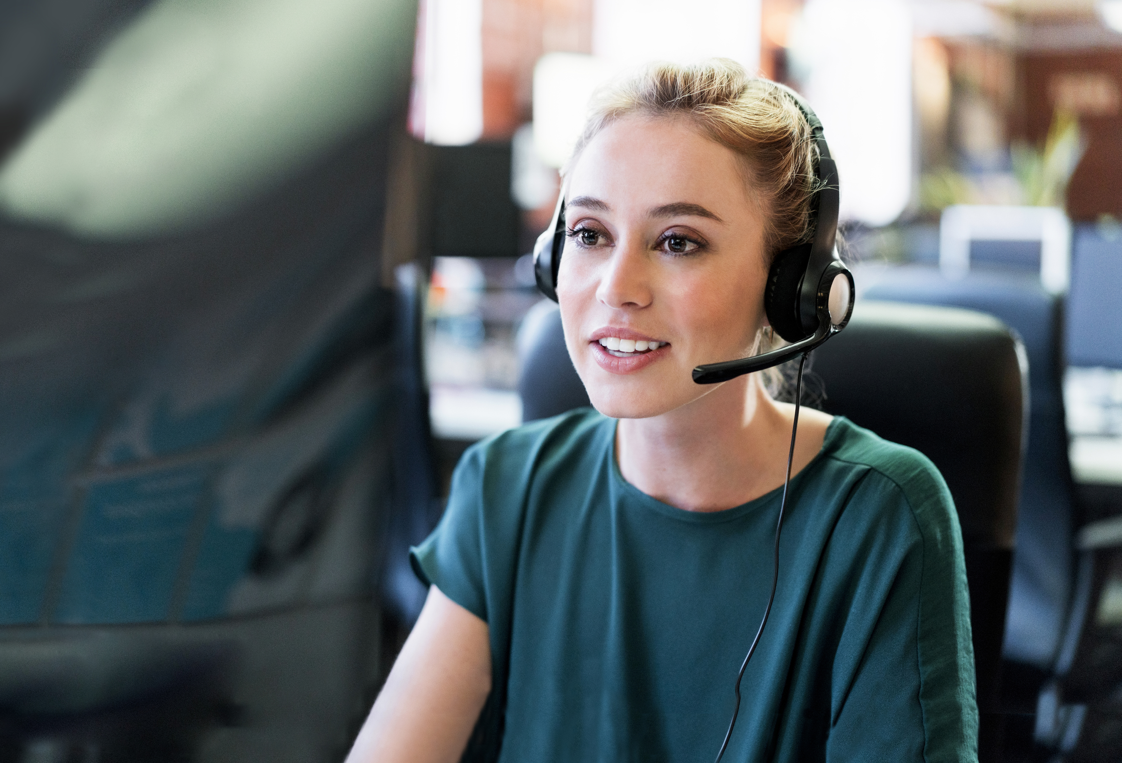 Young and smiling female employee sitting in front of a computer wearing a headset