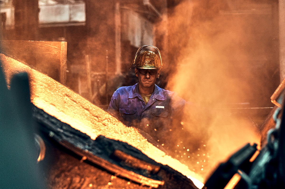 Production specialist in foundry behind a big melting cauldron with glowing copper