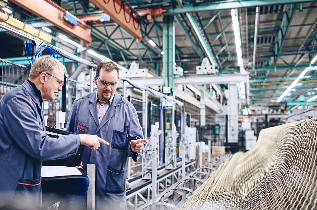 Two engineers wearing safety clothes standing together in a production hall