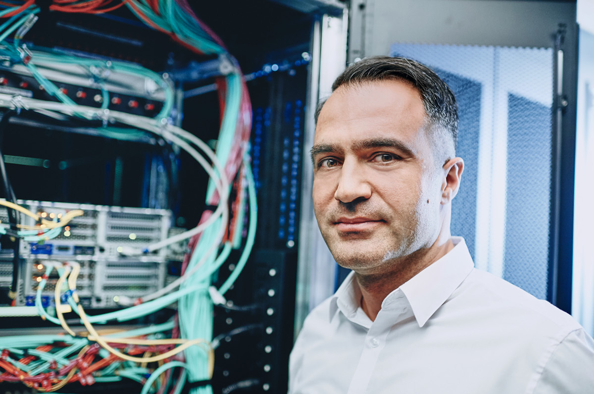IT expert standing in front of a server rack looking into the camera