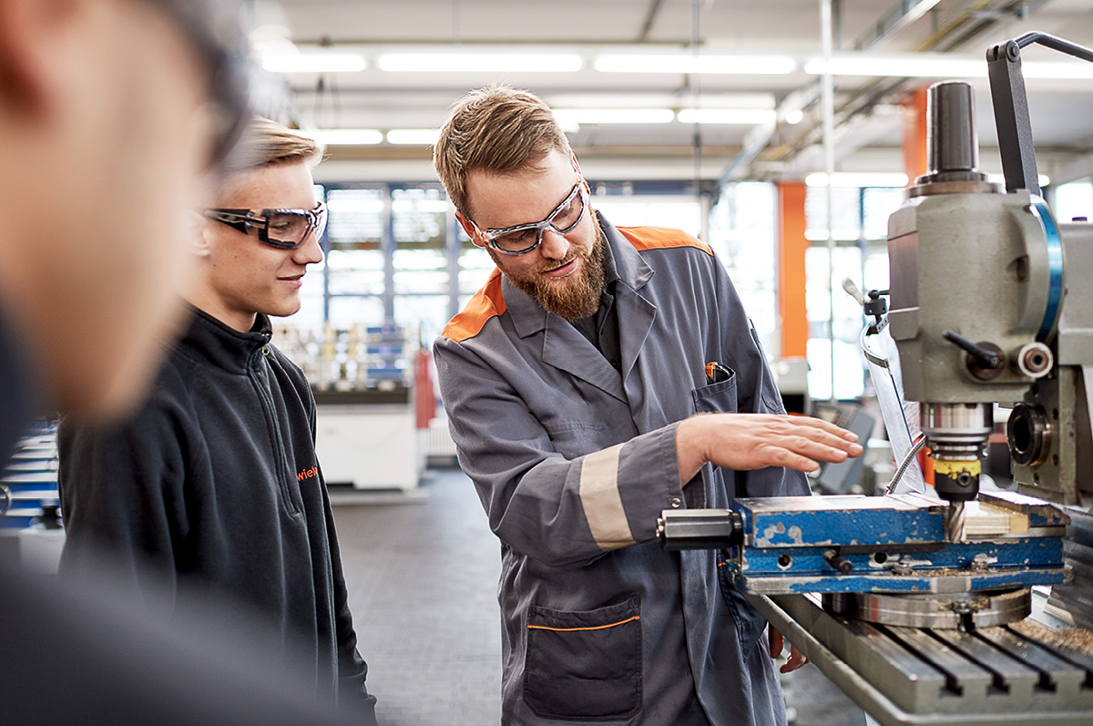 Production specialist showing two trainees how to work on a machine