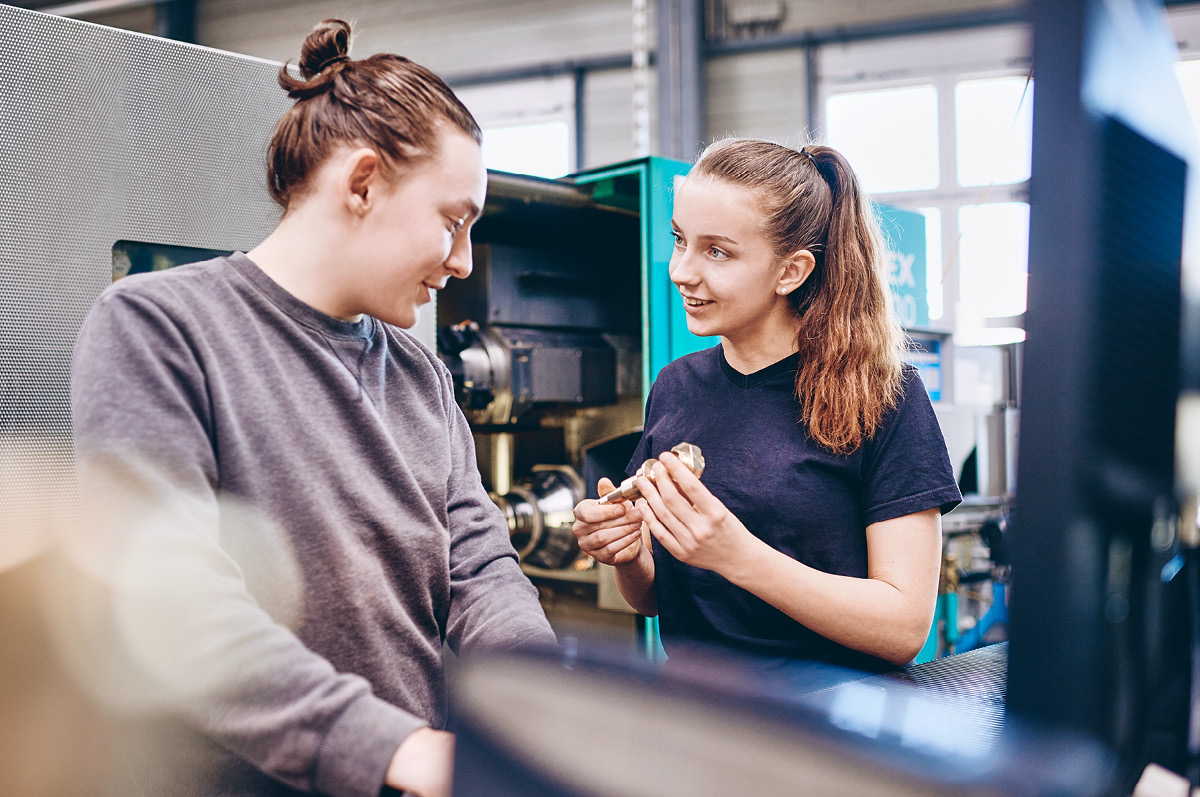 Two young an female trainees talking about a copper component
