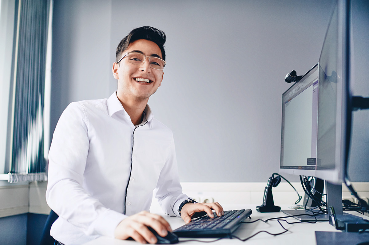 Young male it trainee standing in front of a computer smiling into the camera
