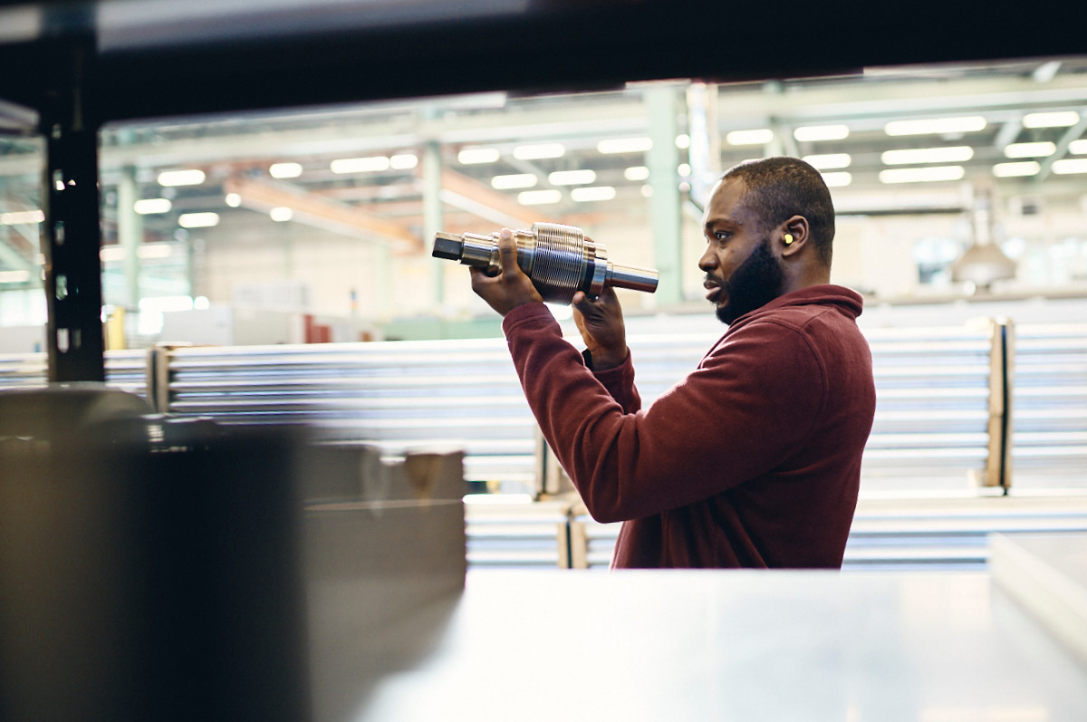 Production specialist wearing hearing protection checking a copper component